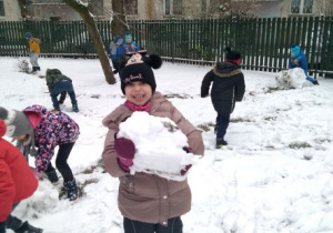 Roześmiana dziewczynka trzyma wielką kulę śniegu
